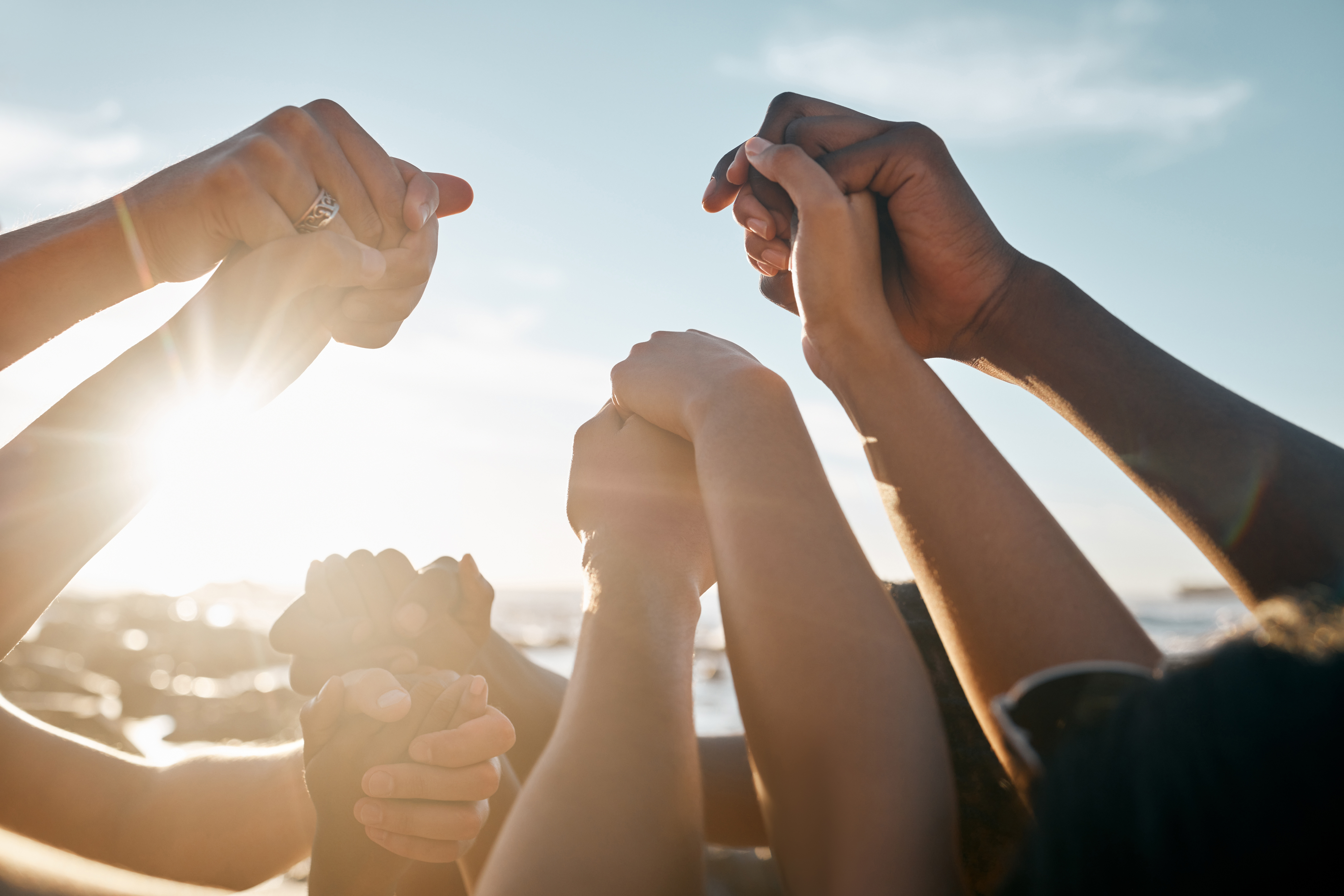 Friends, bonding and holding hands on beach at social gathering, symbolizing peace.